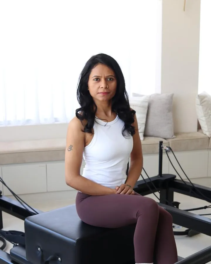 Divya, an Elevate instructor, seated on a reformer in the studio.